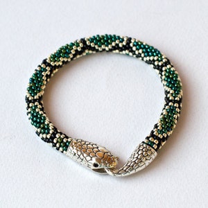Peut inclure: Un bracelet de serpent en perles vertes et noires avec un fermoir en forme de tête de serpent argenté.
