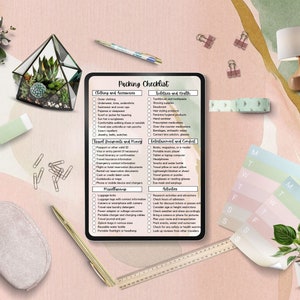 May include: A digital tablet displaying a packing checklist for travel. The checklist includes categories for clothing and accessories, toiletries and health, travel documents and money, entertainment and comfort, activities, and miscellaneous. The tablet is on a pink and green background with a variety of decorative items.