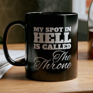 May include: Black coffee mug with white text that reads "My spot in hell is called The Throne".