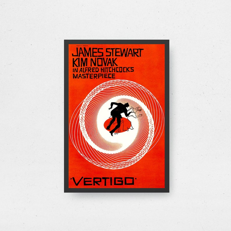 May include: A framed movie poster for the film "Vertigo" featuring James Stewart and Kim Novak. The poster has a vibrant orange background with white spiral lines and a silhouette of a man falling. The film title is at the bottom.
