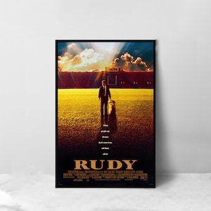 May include: A movie poster for the film "Rudy" featuring a man in a suit standing on a football field with a sunset in the background. The text on the poster reads "When people say dreams don't come true, tell them about Rudy".
