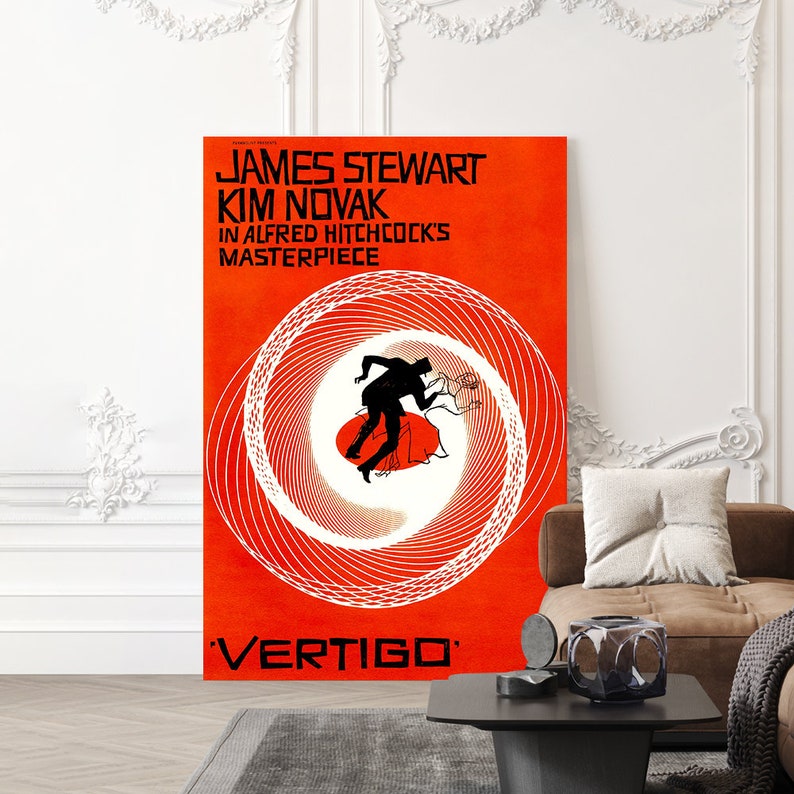 May include: A framed poster for the movie "Vertigo" featuring James Stewart and Kim Novak. The poster has a vibrant orange background with white spiral lines and a silhouette of a man and woman. The movie title is at the bottom.