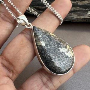 May include: A silver chain necklace with a teardrop-shaped pendant featuring a black and gold pyrite stone.