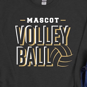 May include: A black sweatshirt with the text "MASCOT VOLLEYBALL" in white and gold lettering. The sweatshirt is laid out on a white surface with a pair of black sneakers, a pair of blue jeans, and a brown leather wallet.