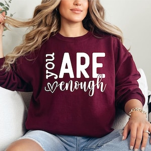 May include: A maroon sweatshirt with the text "You Are Enough" in white lettering with a heart symbol.