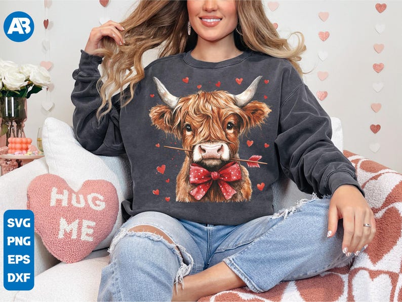Pu&ograve; includere: Una felpa grigia scura con una simpatica illustrazione di una mucca Highland marrone e bianca che indossa un papillon rosso. La mucca tiene una freccia rossa in bocca. La felpa &egrave; circondata da piccoli cuori rossi.