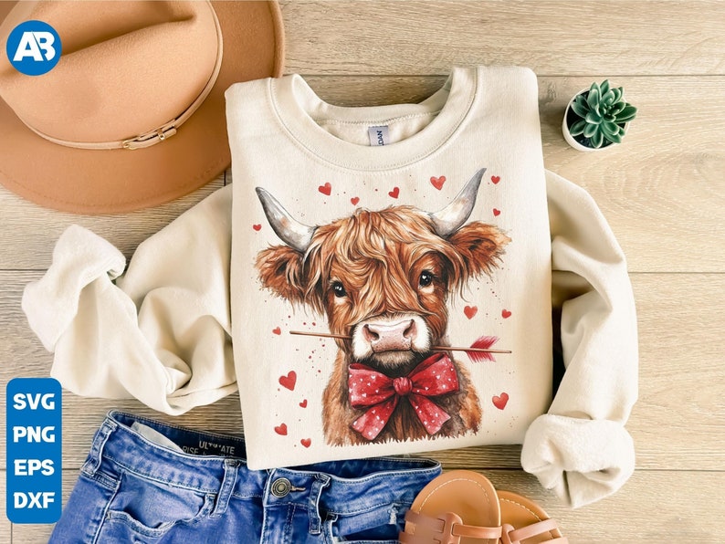 Pu&ograve; includere: Una felpa color crema con una grafica di una mucca Highland marrone e bianca con un papillon rosso e una freccia nel naso. La mucca &egrave; circondata da cuori rossi.
