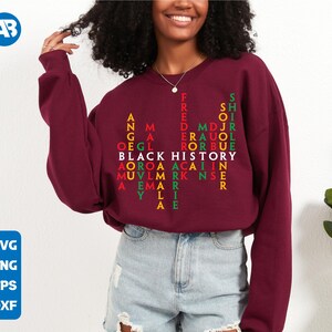 May include: A maroon sweatshirt featuring a red, green and yellow design that spells out "Black History" in a word search puzzle. The design includes names such as "Frederick Douglass", "Martin Luther King Jr." and "Angela Davis".