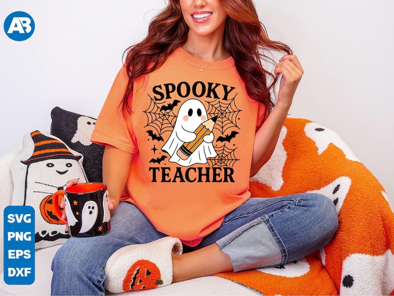 May include: Orange t-shirt with the words "Spooky Teacher" and a cartoon ghost holding a pencil. The design includes bats and a spiderweb. The person is wearing blue jeans and pumpkin-themed slippers.