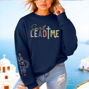 K&ouml;nnte beinhalten: Ein marineblauer Pullover mit dem Text "Spirit Lead Me" in Regenbogenfarben mit einem Kreuz und einem rosa Herzen. Der linke &Auml;rmel tr&auml;gt den Text "Where my trust is without borders" in Regenbogenfarben mit einer Sonnengrafik.