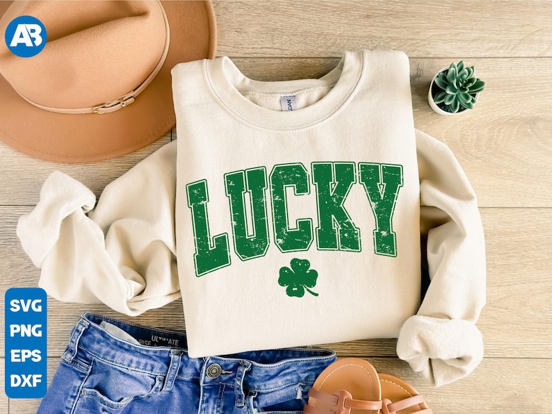 May include: A cream colored sweatshirt with the word "LUCKY" in green distressed lettering. A green four-leaf clover is below the word.