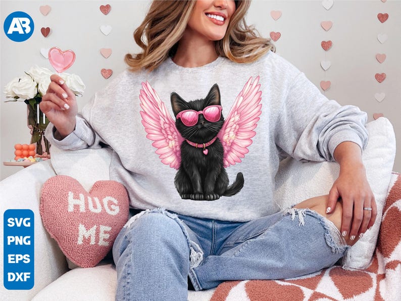 May include: A gray sweatshirt with a black cat wearing pink angel wings and sunglasses. The cat is wearing a pink collar with a heart charm. The text "Hug Me" is on a pink heart-shaped pillow in the background.