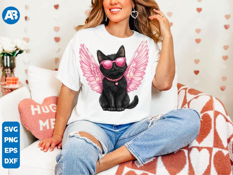 May include: A white t-shirt with a black cat wearing pink angel wings and sunglasses. The cat is sitting on a white background. The t-shirt is being worn by a person.