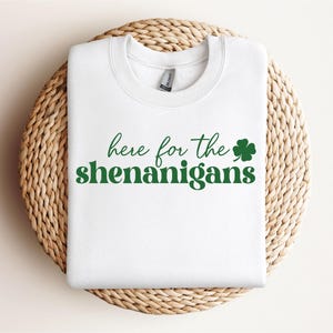May include: White sweatshirt with the text "here for the shenanigans" in green lettering and a green shamrock.