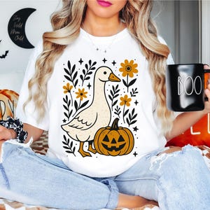 May include: White t-shirt featuring a cartoon goose, a jack-o'-lantern, and floral elements. The design includes the text "Stay Wild Moon Child" and "Boo" on a black mug. The image also shows SVG, PNG, EPS, and DXF file formats.