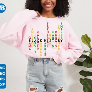 May include: A pink sweatshirt featuring a black, red, green and yellow word puzzle that reads "Black History" in the centre. The puzzle is made up of names of significant African American figures.