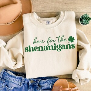 May include: A cream-colored sweatshirt with the text "here for the shenanigans" in green lettering and a green shamrock.