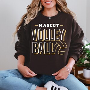 May include: A brown sweatshirt with the text "MASCOT VOLLEYBALL" in white and gold lettering. A volleyball graphic is included in the design.