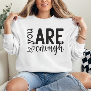 May include: White sweatshirt with the text "You Are Enough" in black lettering with a small heart symbol.