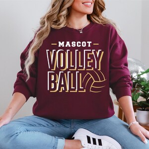 May include: A maroon sweatshirt with the text "Mascot Volleyball" in white and gold lettering. A gold volleyball graphic is to the right of the text.