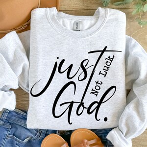 May include: A gray sweatshirt with the text "just God. Not Luck." in black cursive lettering.