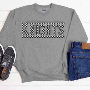May include: Gray sweatshirt with the word "KNIGHTS" in black letters with a checkered pattern.