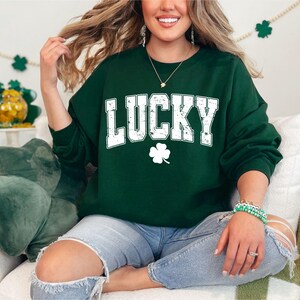 May include: A green sweatshirt with the word "LUCKY" in white letters with a distressed look. A white four-leaf clover is below the word.