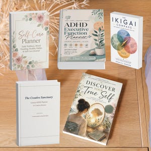 Puede incluir: Cinco libros con diversos diseños de portada. Los títulos incluyen Self-Care Planner, ADHD Executive Function Planner, The Ikigai Compass, The Creative Sanctuary Luxury ADHD Planner y Discover Your True Self, con arte floral y abstracto.