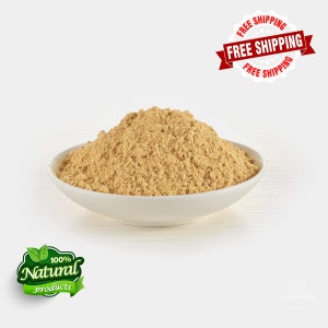 May include: A white bowl containing a light brown powder, possibly a spice or supplement. The bowl is centrally positioned against a white backdrop. A green and white label reads "100% Natural products". A red banner with "FREE SHIPPING" is in the top right.