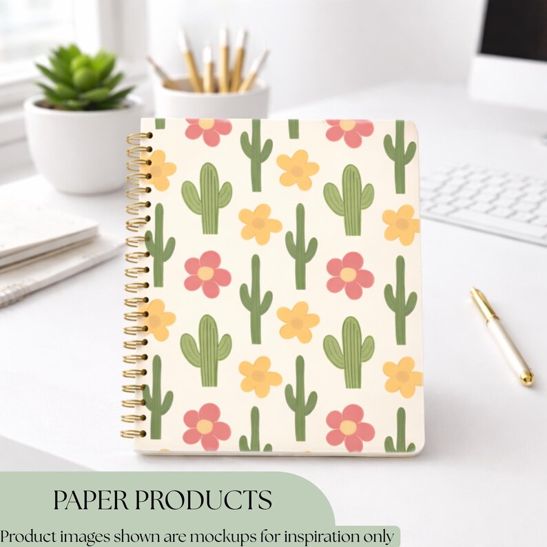K&ouml;nnte beinhalten: Ein cremefarbenes Spiralnotizbuch mit einem sich wiederholenden Muster aus gr&uuml;nen Kakteen, rosa und gelben Blumen. Das Notizbuch hat eine goldene Spiralbindung. Der Text "PAPER PRODUCTS" befindet sich am unteren Rand des Bildes.