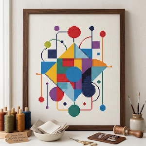 Könnte beinhalten: Ein gerahmtes Kreuzstich-Kunstwerk mit einem abstrakten geometrischen Design mit bunten Formen. Das Design umfasst rote, gelbe, blaue, grüne und violette Elemente. Der Rahmen ist aus dunklem Holz. Der Text auf dem Etikett lautet: Design Size 100x120 Stitches, 14ct Aida.