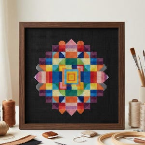 May include: A framed cross-stitch artwork featuring a geometric, mandala-like design. The design is composed of various colorful squares in shades of red, orange, yellow, green, blue, and purple, set against a black background. The frame is made of dark wood.