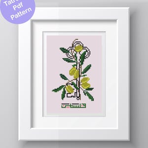May include: A framed cross-stitch pattern featuring a stylized olive branch with yellow olives and green leaves. The design includes Arabic text in green and is set against a light pink background. The frame is white, and the text "Tatreez Pdf Pattern" is in a purple circle.