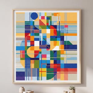 May include: A framed cross-stitch artwork featuring an abstract geometric design. The artwork uses a variety of colors, including blue, orange, red, and yellow, arranged in a patchwork style. The piece is displayed in a light-colored wooden frame.