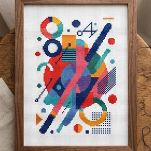Può includere: Un'opera d'arte a punto croce incorniciata con un design geometrico astratto. Il design incorpora cerchi, quadrati e linee diagonali in una vivace tavolozza di colori. La cornice è in legno. Un oggetto artigianale decorativo.