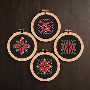 Puede incluir: Cuatro aros de bordado con tela negra y diseños florales rojos y verdes. Los diseños son geométricos y simétricos.