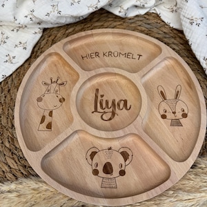 Könnte beinhalten: Ein geteilter Holzteller mit Giraffe, Hase und Koala-Motiv. Der Teller ist mit dem Text "Hier Krümelt" und dem Namen "Liya" graviert.
