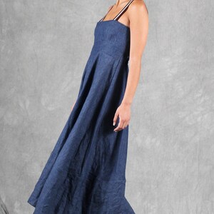 May include: A floor-length navy blue dress with a square neckline and thin, striped shoulder straps. The garment features a fitted bodice that transitions into a full, flowing skirt with a visible seam at the hemline, crafted from a textured fabric.