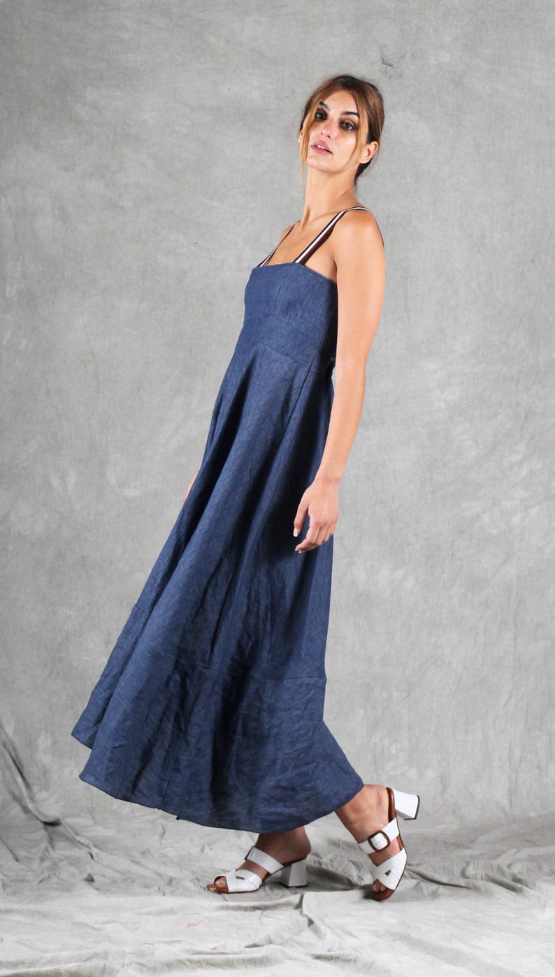 May include: A floor-length navy blue dress with a square neckline and thin, striped shoulder straps. The garment features a fitted bodice that transitions into a full, flowing skirt with a visible seam at the hemline, crafted from a textured fabric.