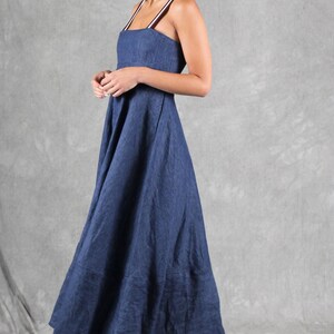 May include: A floor-length navy blue dress with a square neckline and thin, striped shoulder straps in white, brown, and black. The garment features a fitted bodice that transitions into a full, flowing skirt, paired with white block-heeled sandals.
