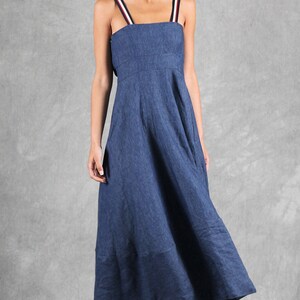 May include: A long blue dress with a square neckline and shoulder straps featuring red, white, and navy blue stripes. The dress has a fitted bodice and a flowing skirt that reaches below the knees, paired with white open-toe sandals with buckles.
