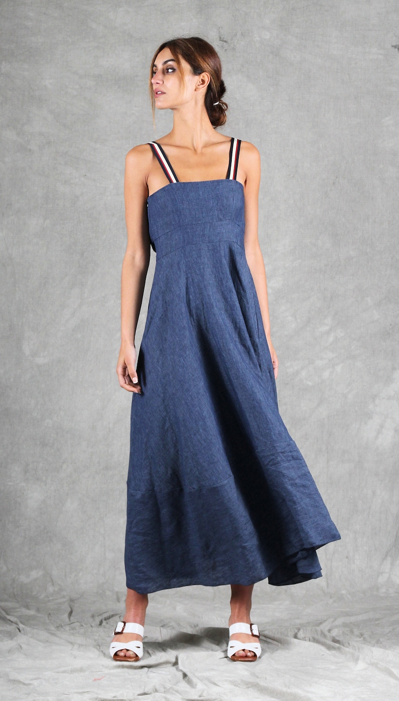 May include: A long blue dress with a square neckline and shoulder straps featuring red, white, and navy blue stripes. The dress has a fitted bodice and a flowing skirt that reaches below the knees, paired with white open-toe sandals with buckles.