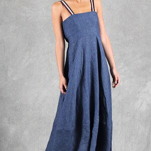 May include: A blue midi-length dress with a square neckline and shoulder straps featuring red, white, and black stripes. The dress has a fitted bodice and a flared skirt. It is paired with white open-toe sandals with a brown sole and buckle detail.