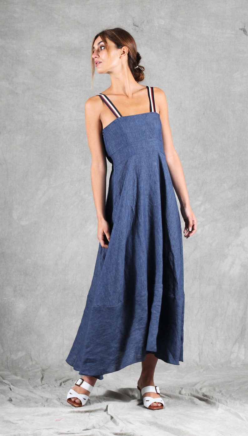 May include: A blue midi-length dress with a square neckline and shoulder straps featuring red, white, and black stripes. The dress has a fitted bodice and a flared skirt. It is paired with white open-toe sandals with a brown sole and buckle detail.