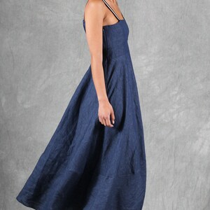 May include: A dark blue midi dress with a square neckline and thin shoulder straps featuring a white stripe detail. The dress has a fitted bodice and a flared skirt that falls below the knee. The garment is paired with white heeled sandals.