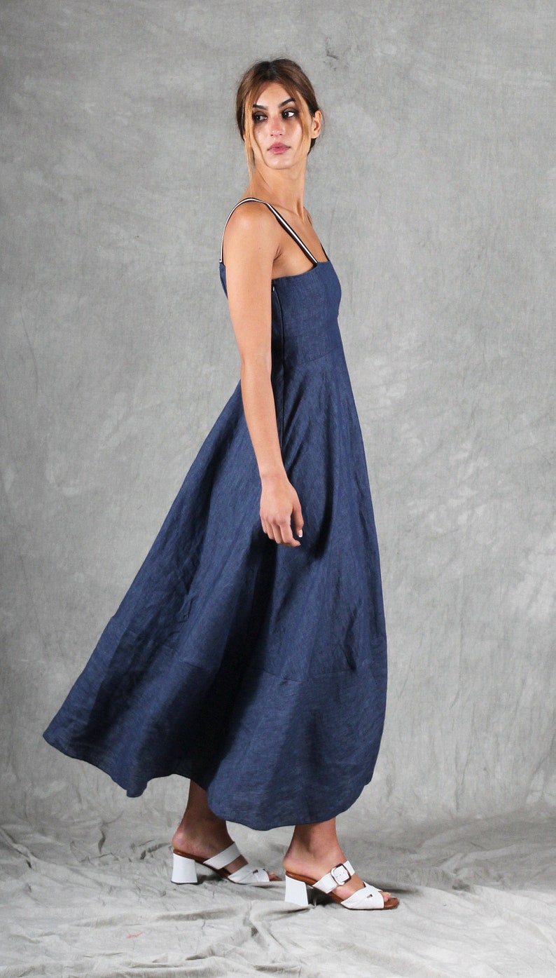 May include: A dark blue midi dress with a square neckline and thin shoulder straps featuring a white stripe detail. The dress has a fitted bodice and a flared skirt that falls below the knee. The garment is paired with white heeled sandals.