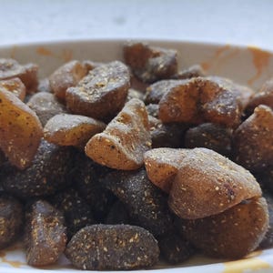 以下が含まれることがあります： 白磁のボウルに、茶色と黒のキャンディーの塊が入っています。キャンディーの塊は不規則な形をしていて、ざらざらした質感です。