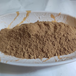 Puede incluir: Primer plano de un plato blanco con un montón de polvo marrón. El plato tiene un diseño de mármol dorado.