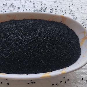 May include: A white ceramic bowl filled with black nigella seeds.