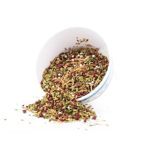 May include: A white bowl filled with a mixture of green, red, and white spices. The bowl is tipped over and the spices are spilling out onto a white surface.